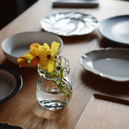 A clear glass vase with a rounded bulbous base and slender neck holds yellow flowers as decorbites geometric square vase