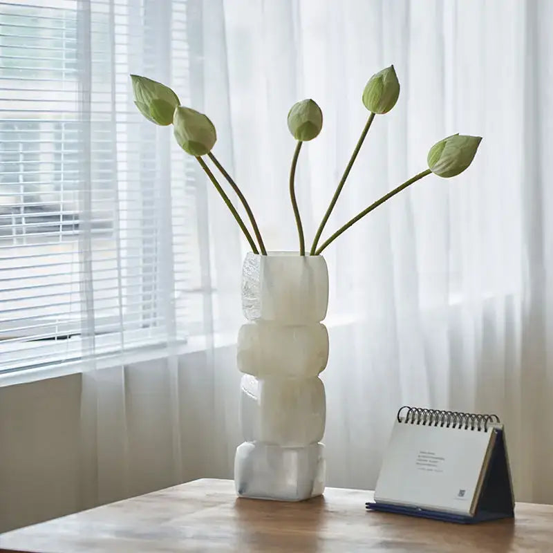 Glossy white geometric square vase decorbites holds green lotus buds in a translucent stacked block square vase table setting