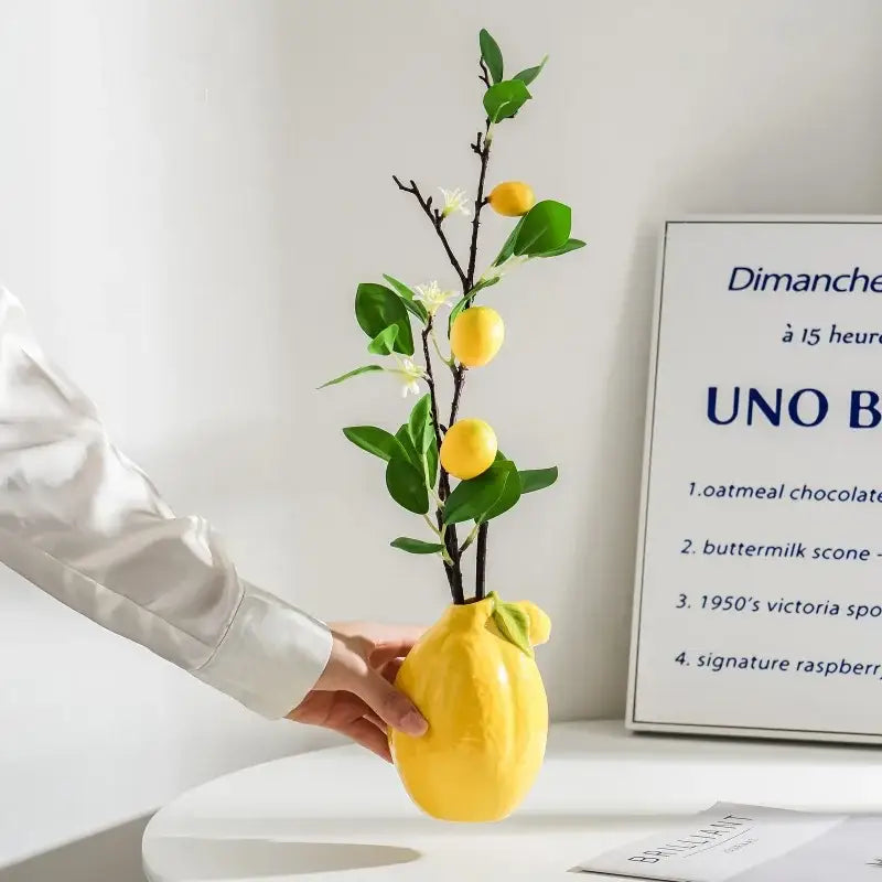 Glossy yellow ceramic lemon flower vase by decorbites holding a decorative citrus branch with small lemons and leaves