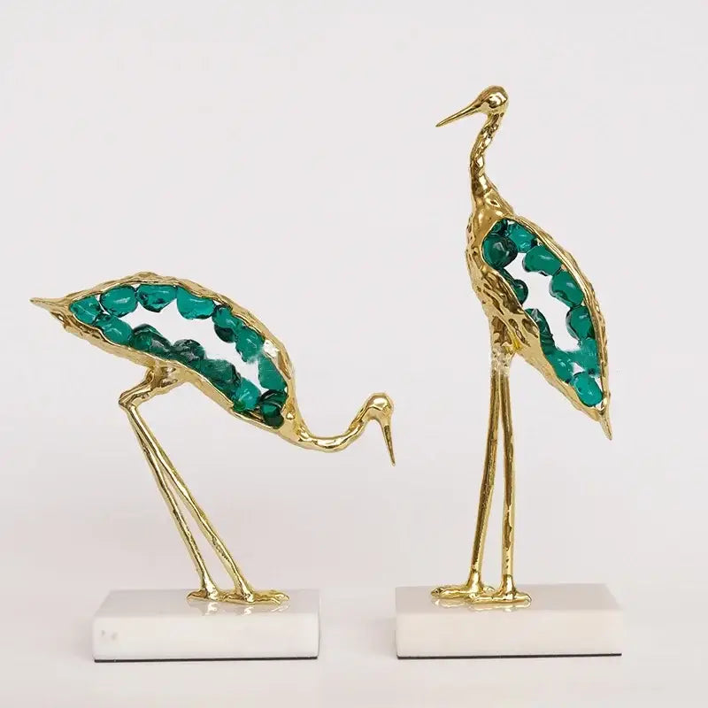 Gold and emerald crystal crane sculpture featuring golden crane figurines with emerald wings on white marble bases for decor