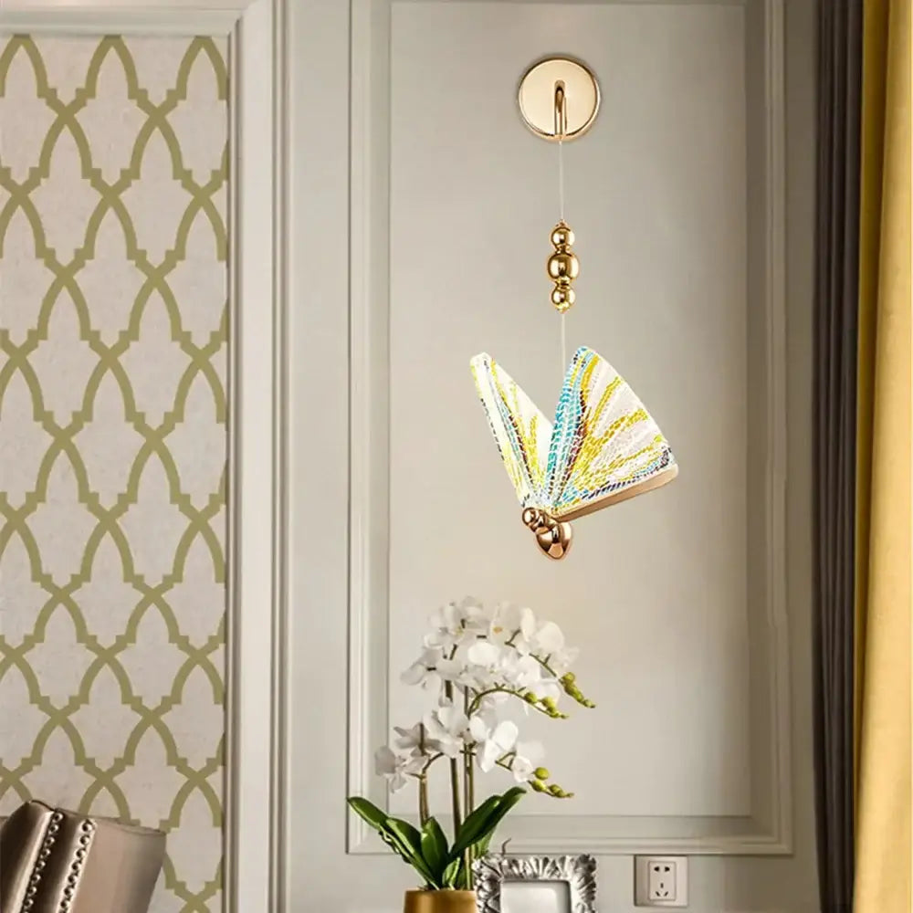 Gold and patterned butterfly led wall light with iridescent yellow blue wings suspended by gold chain ceiling mount