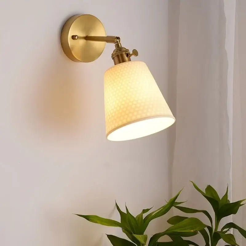 Gold and white ceramic LED wall sconce with warm-toned brass base and textured off-white fabric shade by decorbites