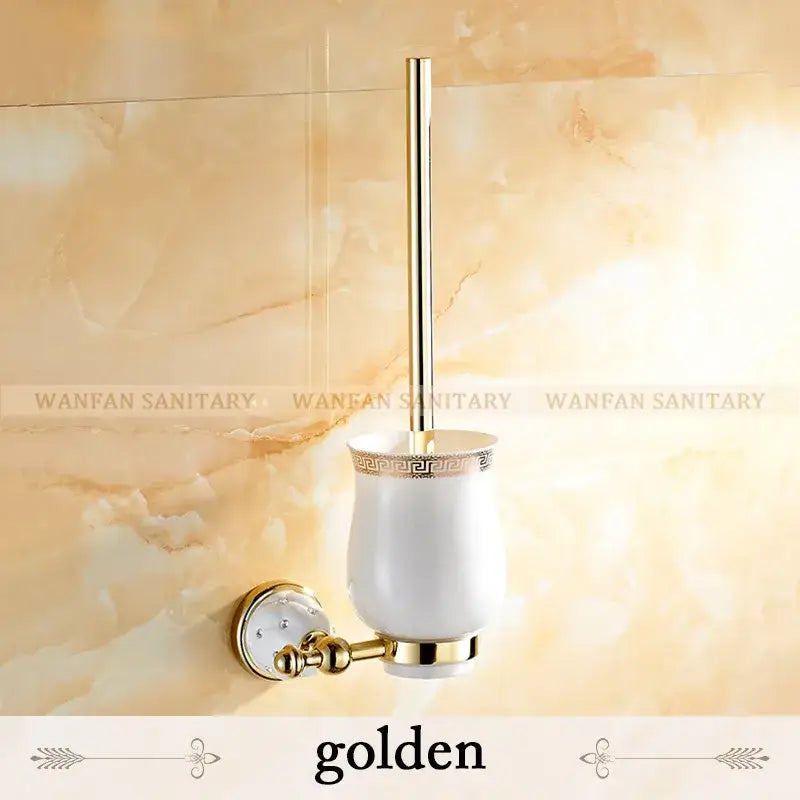 Gold-finished toilet brush holder with white ceramic cup and ornate greek key pattern in a bath hardware set