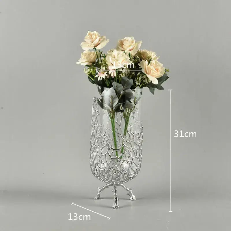 A tall glass vase with silver lattice and ornate feet holding cream roses complements gold coral crystal tree decor