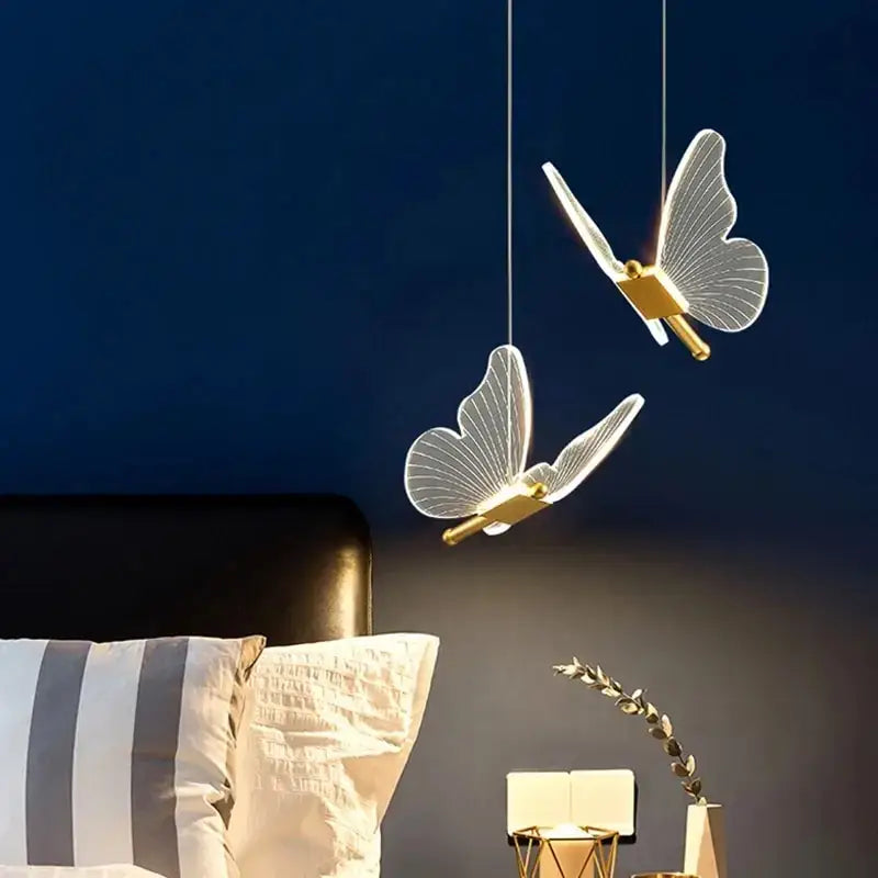 Two elegant translucent butterfly-shaped gold metal pendant lights hang against a dark blue bedroom wall
