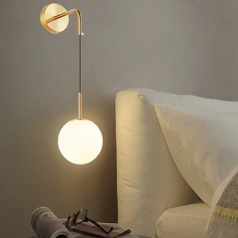 Gold-toned light fixture with opal glass spherical shade and sleek curved arm for bedroom wall mounting