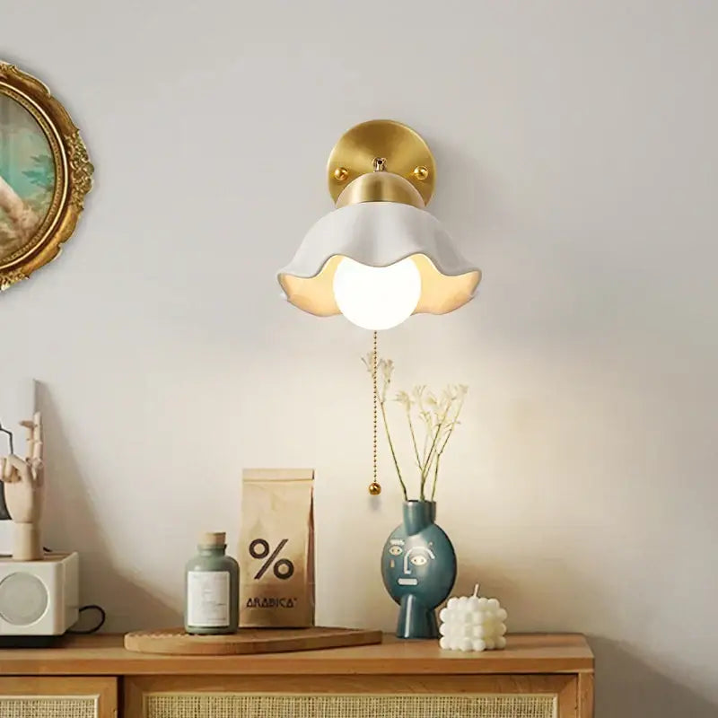 Delicate white ceramic wall light fixture with gold-toned metal base and petal-like shade with pull chain switch