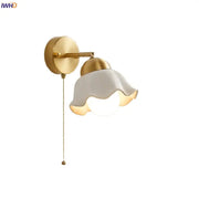 Gold-toned wall light fixture with white ruffled glass shade and attached pull chain for bedroom lighting