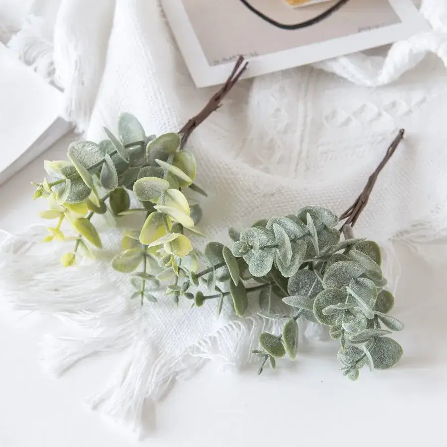 Faux eucalyptus leaves with frosted green foliage and brown stems arranged on white fabric for decorbites eucalyptus leaves artificial plants decor