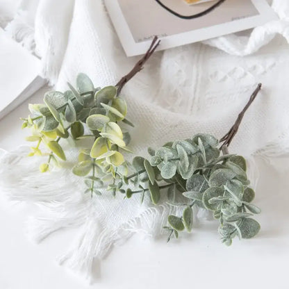 Faux eucalyptus leaves with frosted green foliage and brown stems arranged on white fabric for decorbites eucalyptus leaves artificial plants decor