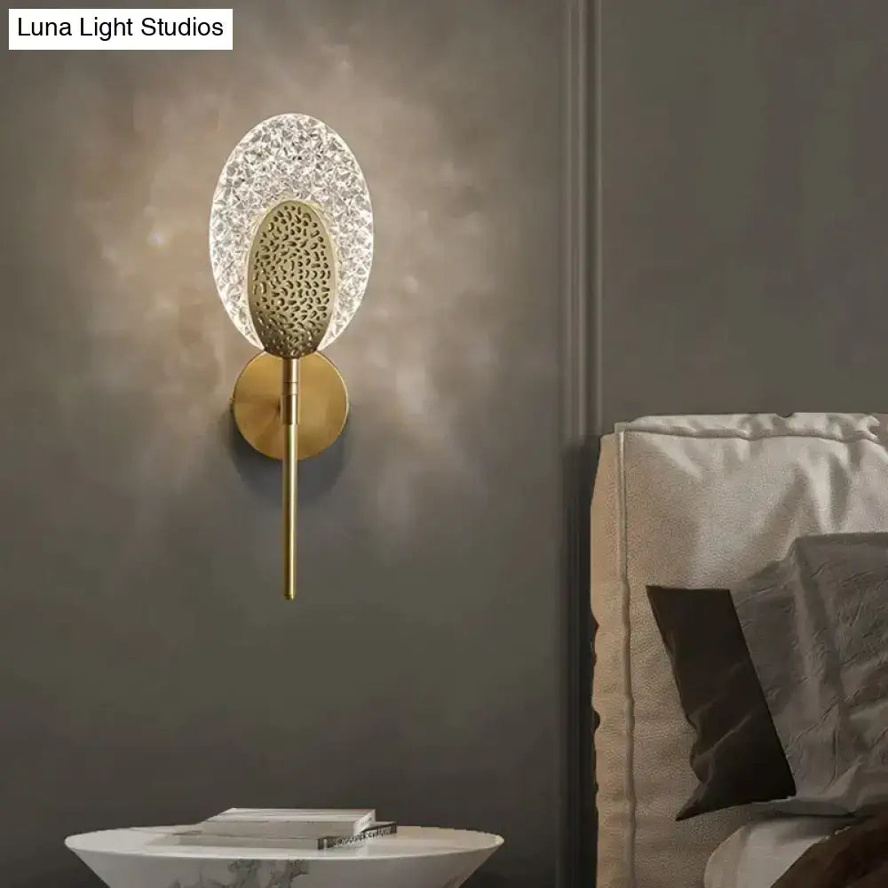 Gold-toned led wall lamp with textured oval glass diffuser and intricate central design for indoor lighting in bedroom