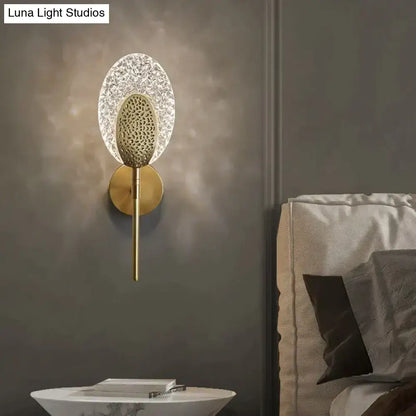 Gold-toned led wall lamp with textured oval glass diffuser and intricate central design for indoor lighting in bedroom