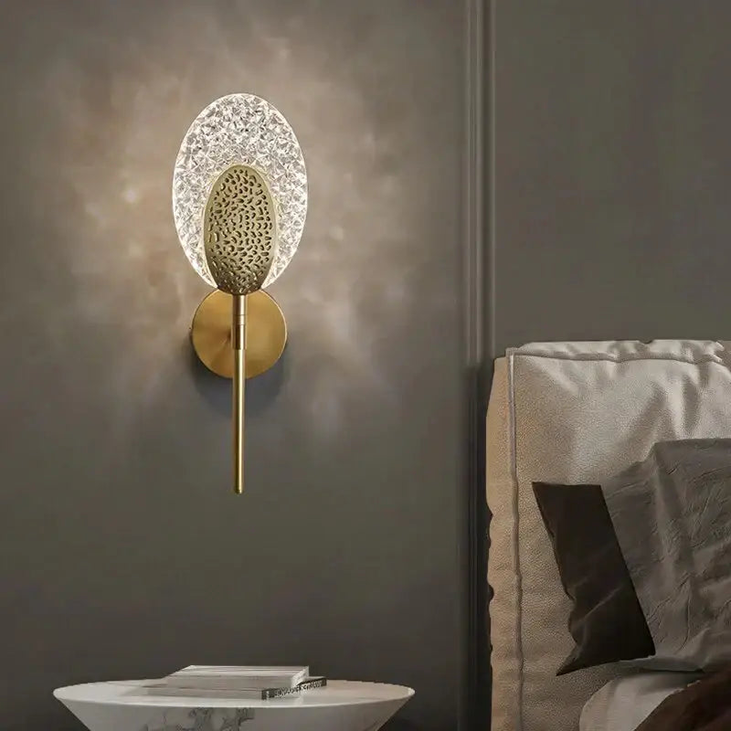 Gold-toned led wall lamp with textured oval glass diffuser and intricate central element for indoor lighting use
