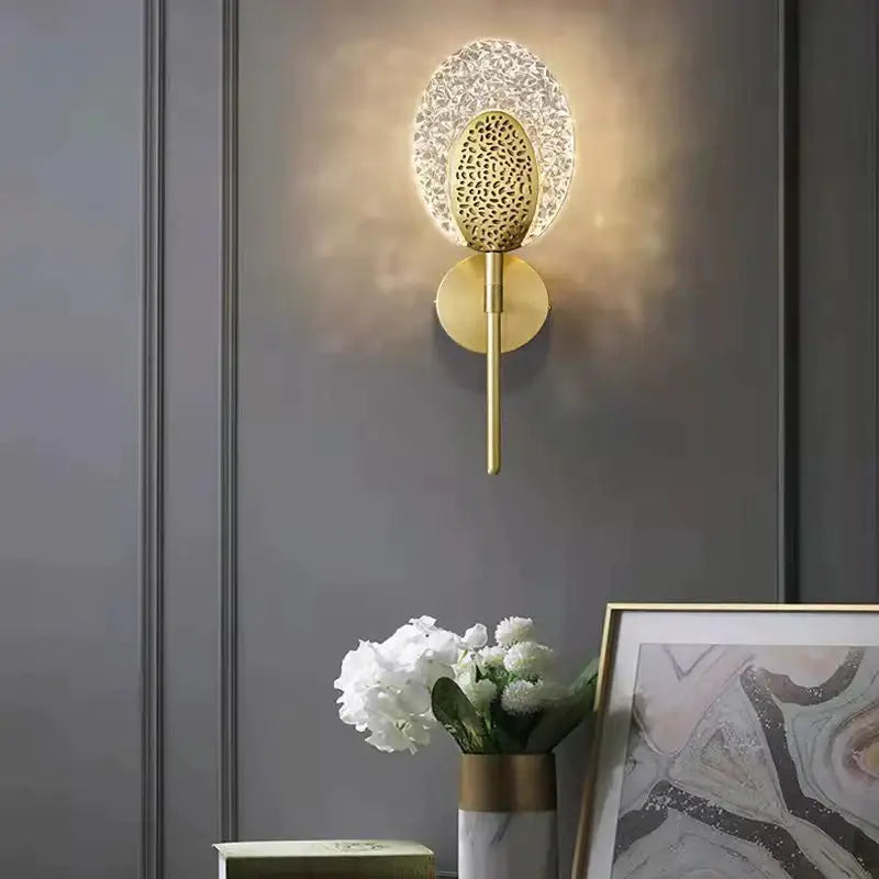 Gold-toned led wall lamp with textured glass shade and patterned metal center for indoor lighting in bedroom