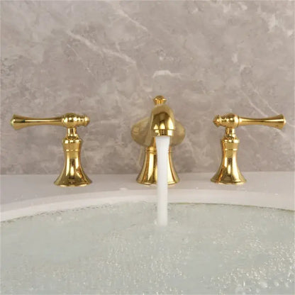 Gold widespread bathroom faucet with three gold finished lever handles and waterfall design set against marble backsplash