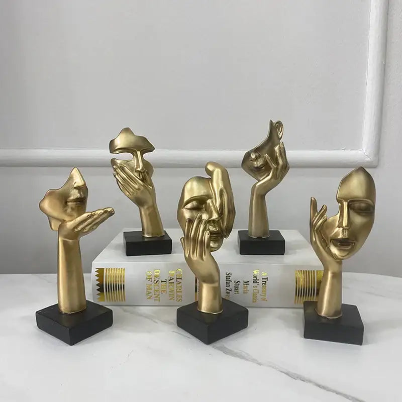 Golden abstract mask statue featuring metallic hand and face sculptures with sleek designs on black bases for decor