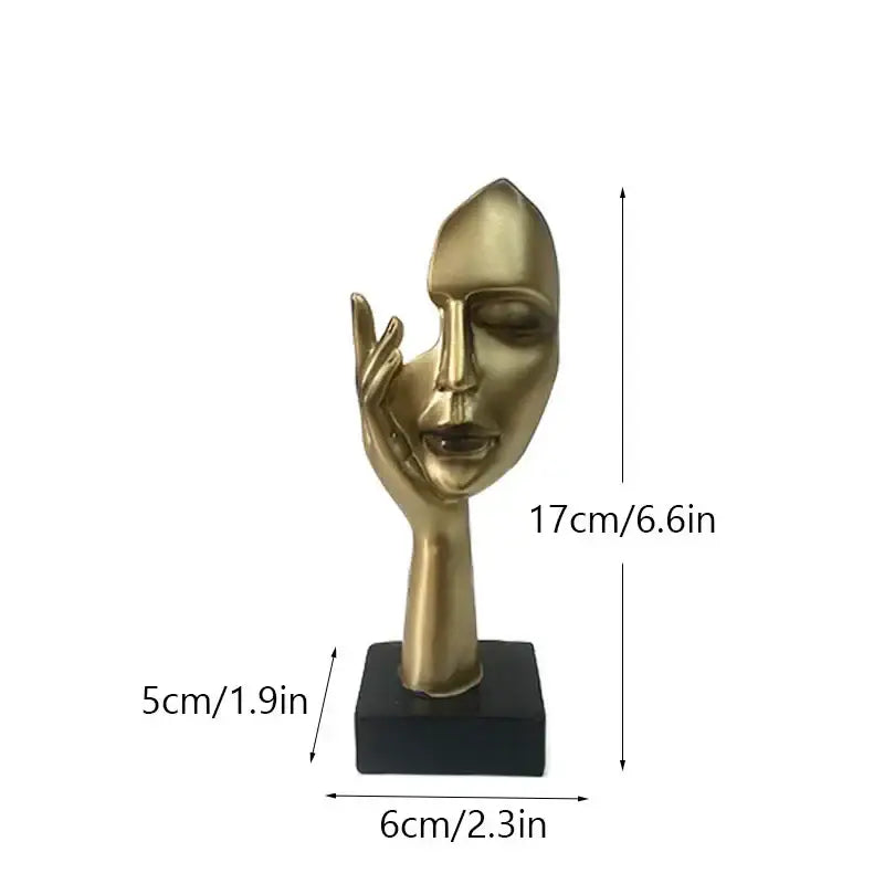 Golden metallic abstract mask statue with stylized face and hand on cheek on black base for home office decor