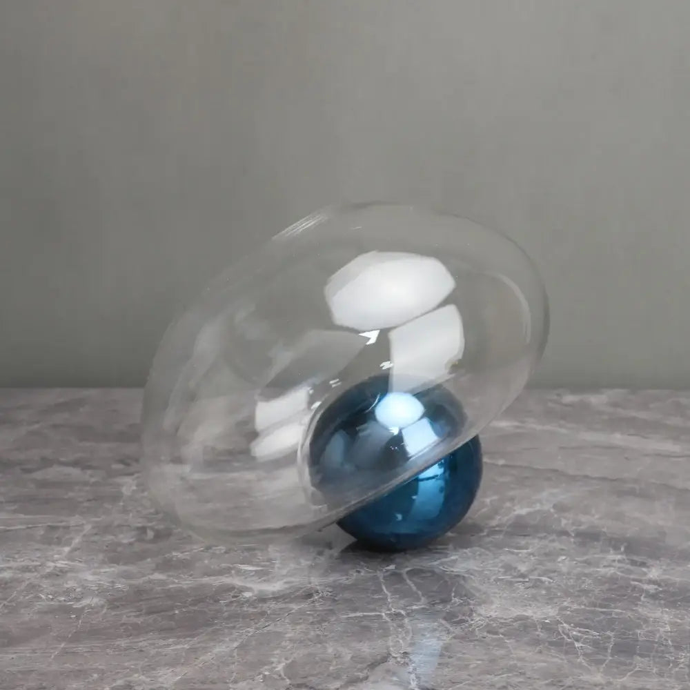A translucent glass dome cradles a glossy blue spherical ornament in a decorbites golden ball glass vase