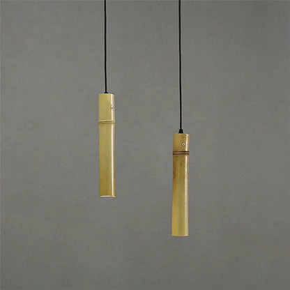 Two slender golden bamboo tube pendant lights with adjustable wire hang against a neutral gray backdrop for dining rooms