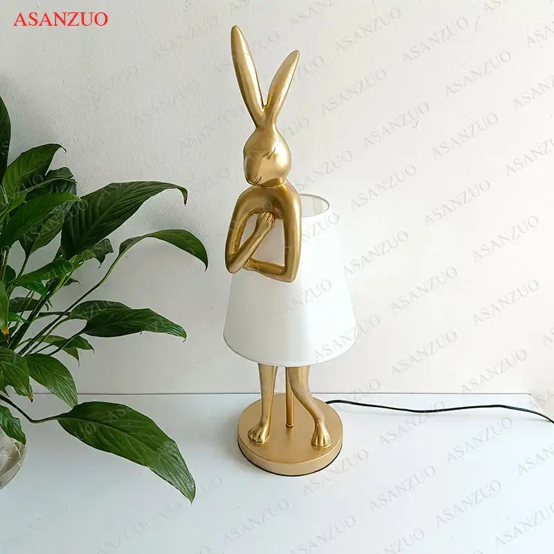 Gold-colored bathing rabbit resin table lamp with white conical shade and circular base for bedroom decorbites decor
