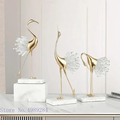 Three elegant gold-colored golden bird agate crane statues with crystal feathers on white bird agate marble bases for home decor