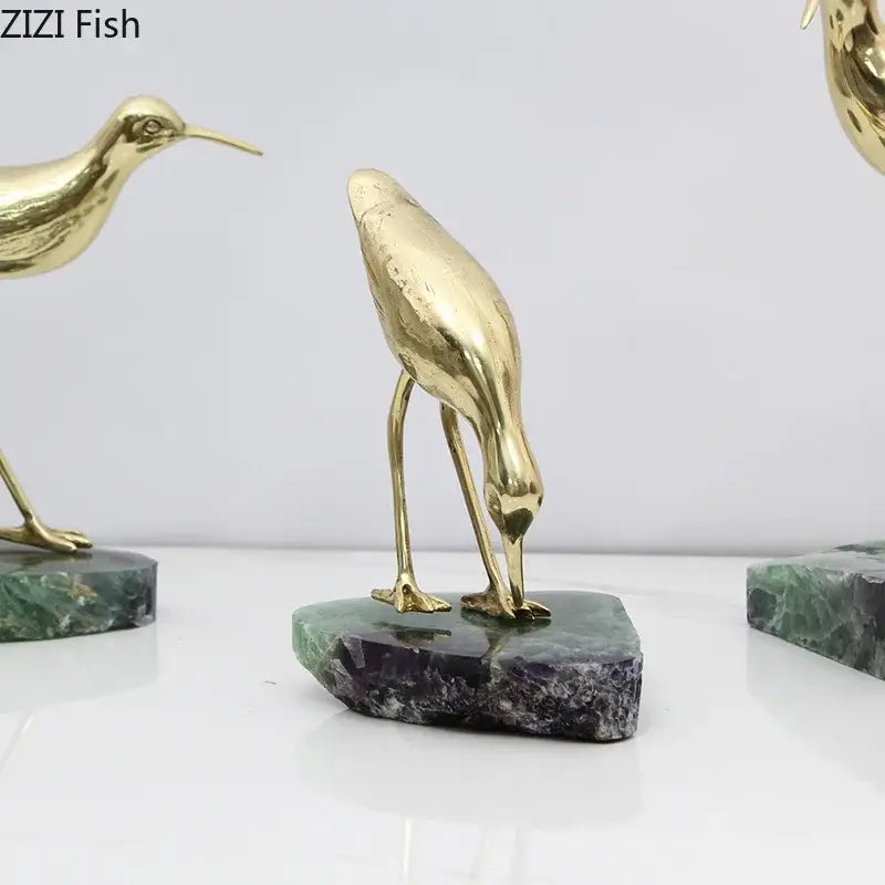 Golden brass bird desk ornament with slender legs and long beak on polished green and purple marble base
