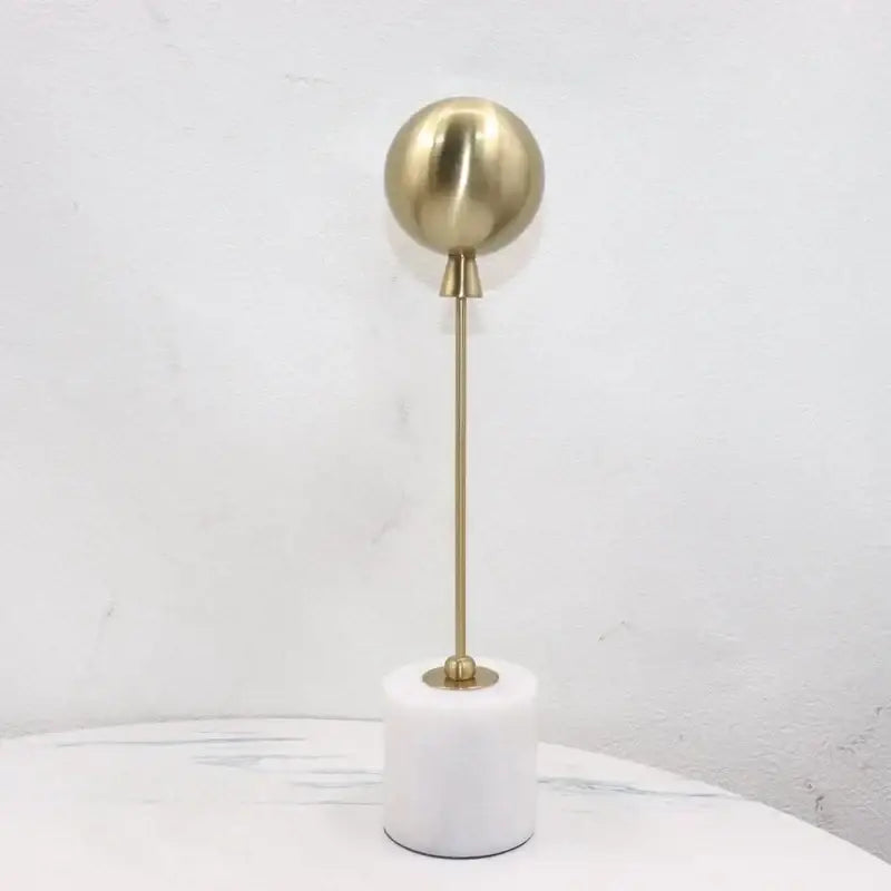 A sleek golden geometric balloon metal ball sculpture with a brass sphere on a white marble base for decorbites decor