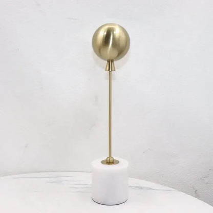 A sleek golden geometric balloon metal ball sculpture with a brass sphere on a white marble base for decorbites decor