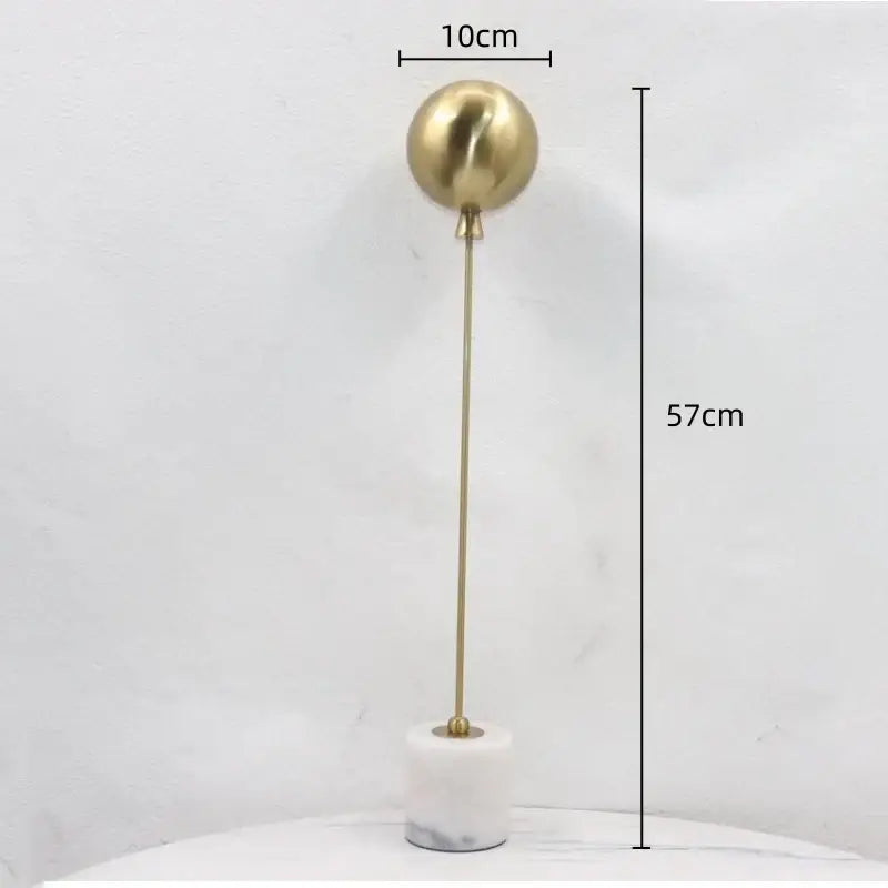 A sleek gold-toned spherical metal ball sculpture on a white marble base for golden geometric balloon living room decor