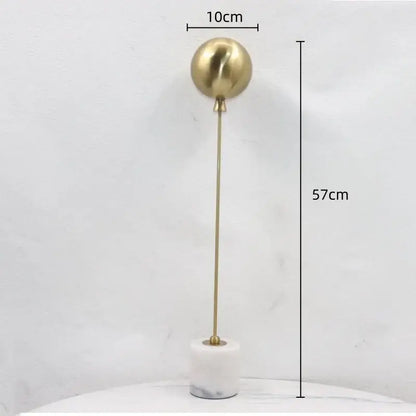 A sleek gold-toned spherical metal ball sculpture on a white marble base for golden geometric balloon living room decor