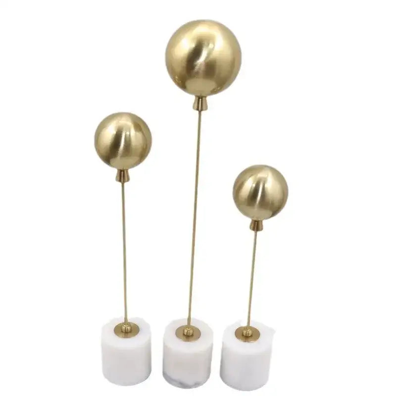 Set of three golden geometric balloon metal ball sculptures with slender stems and white marble bases for living room decor