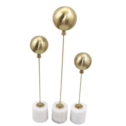 Set of three golden geometric balloon metal ball sculptures with slender stems and white marble bases for living room decor