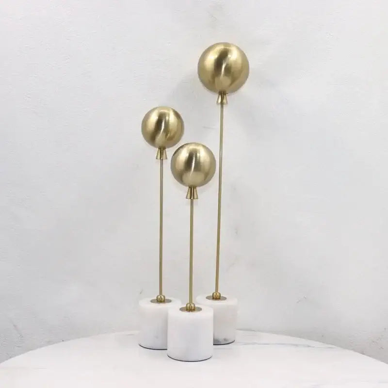 Set of three golden geometric balloon metal ball sculptures on white marble bases for living room decorbites decor