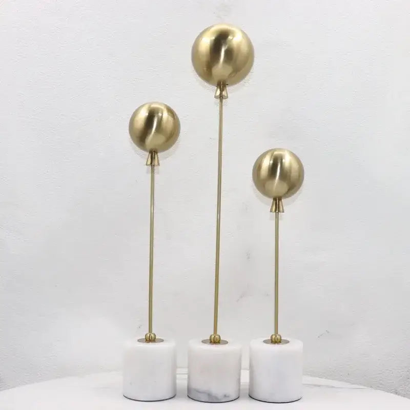 Set of three golden geometric balloon metal ball sculptures on white marble bases for living room decorbites decor