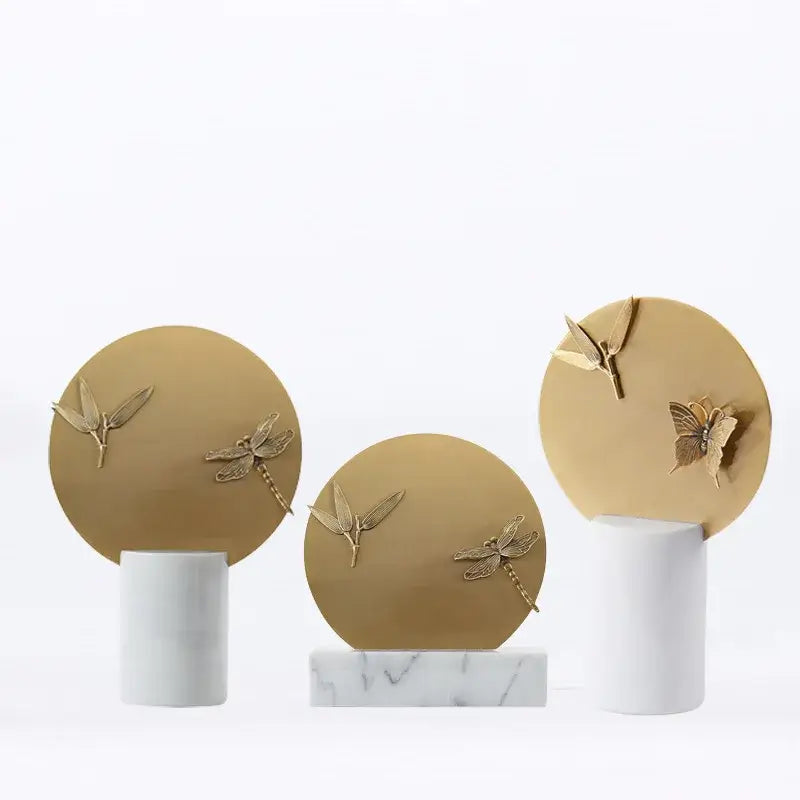 Golden geometric insect figurine set with gold-toned circular plaques embossed with dragonfly and leaf motifs on marble bases home decor