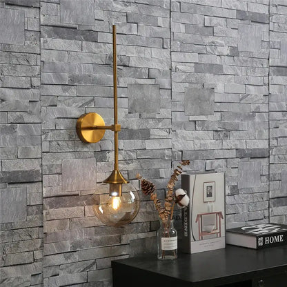Golden glass ball led wall light bedroom brass sconce with a gold-toned slender arm and spherical glass bulb by decorbites
