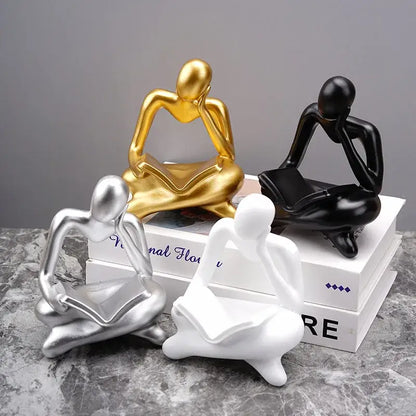 Set of four glossy resin figurines in gold black silver and white depicting the decorbites abstract thinker design
