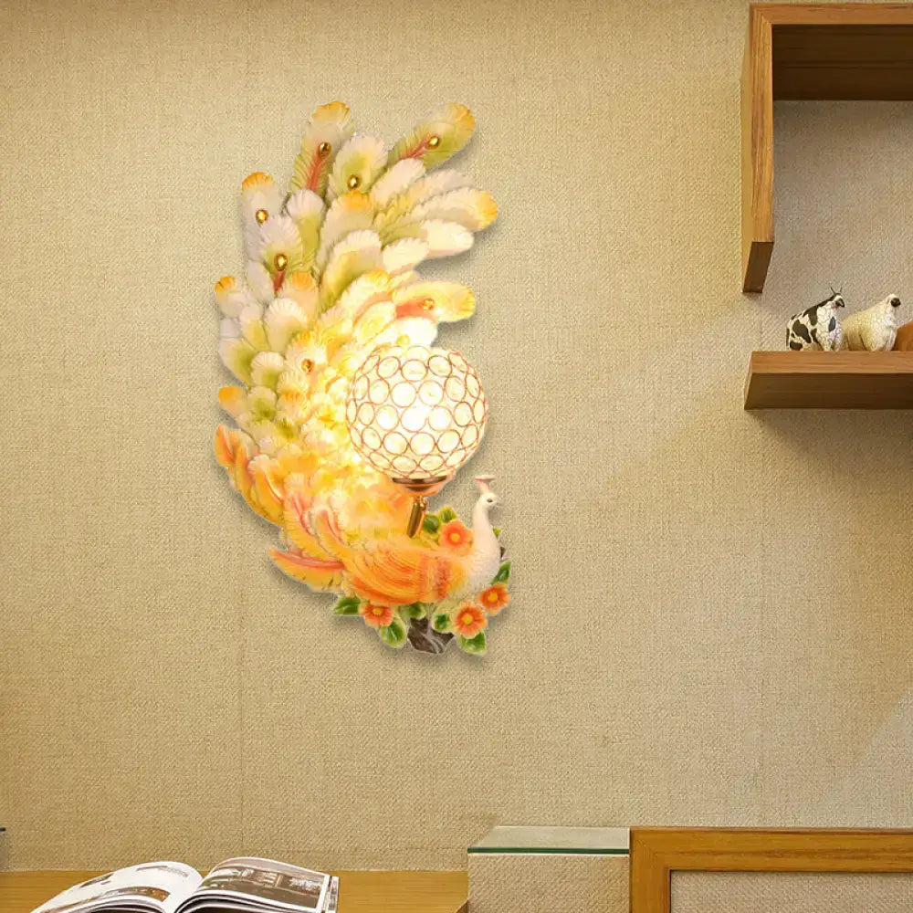 Golden peacock wall light with crystal shade featuring vibrant yellow green feathers and a glowing spherical lampshade