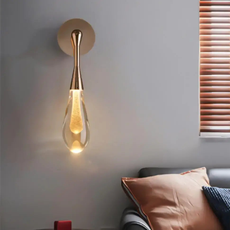 A modern decorbites golden water wall light with a gold-toned frame and teardrop-shaped glass shade emitting warm light