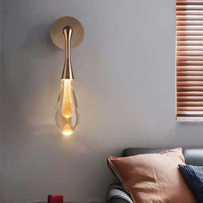 A modern decorbites golden water wall light with a gold-toned frame and teardrop-shaped glass shade emitting warm light