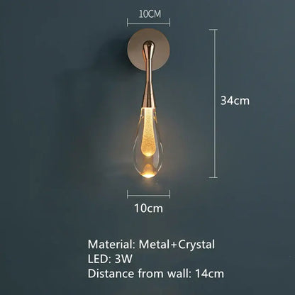 A sleek teardrop-shaped bedroom wall light with brass metal stem and clear crystal body with golden led light decorbites golden water droplets