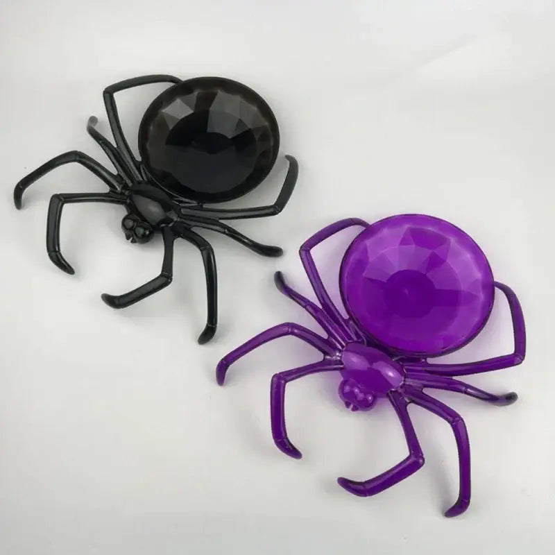 Two plastic spider-shaped pins in black and purple with faceted gemstone bodies for skull spider tray decor