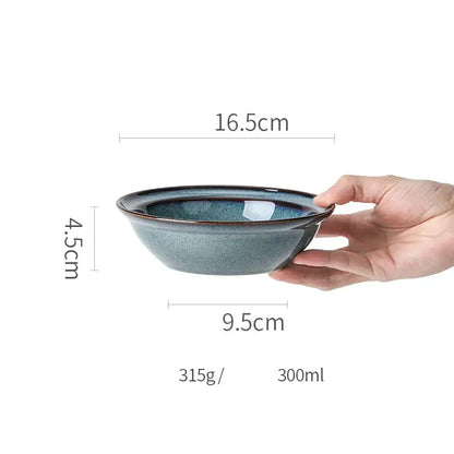 A hand holds a beautiful blue ceramic bowl with deep glaze and dark rim dinnerware dish for dining room use