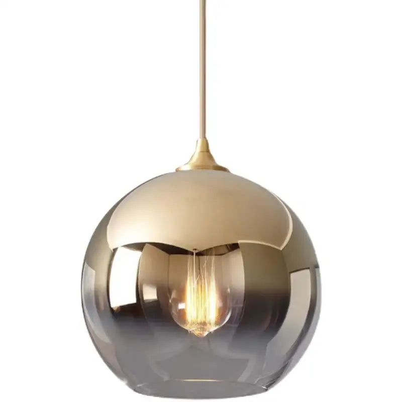 A sleek spherical gradient glass ball pendant light with brushed gold finish and exposed filament bulb for dining room