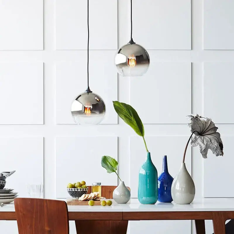 Two spherical chrome-finished gradient glass ball pendant lights hang from black cords on white paneled wall