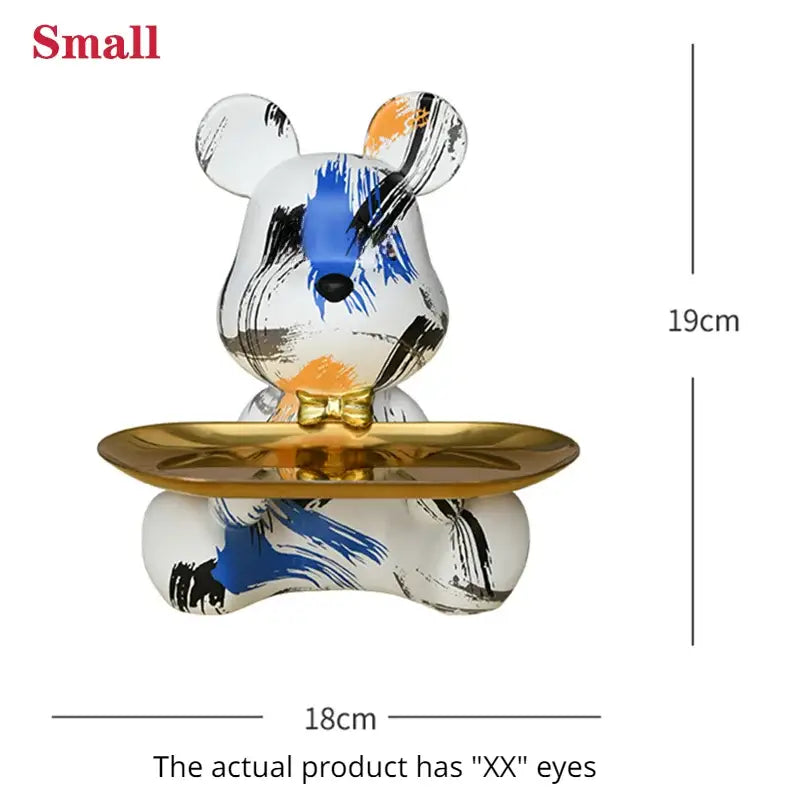 A small white ceramic bear figurine with blue and black graffiti patterns wearing a gold bow tie holding a gold tray