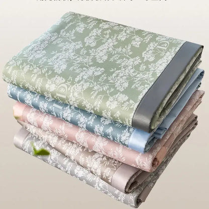Stacked satin-like bed mat set in soft gray and lavender with delicate white floral patterns and solid-colored borders