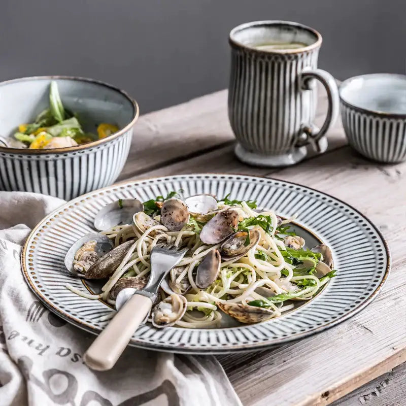 A gray and white striped ceramic wedding tableware set plate with textured rim serving clams over pasta by decorbites ceramic wedding