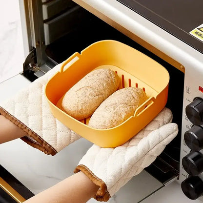 Yellow rectangular baking tray with handles and slotted base holding bread loaves for green and black silicone air fryer pot baking tray
