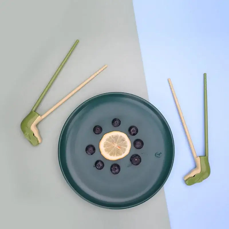 Dark green ceramic plate with sliced lemon blueberries shown with green dino chopsticks kids training set decorbites